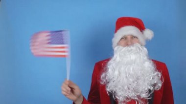 Mavi arka planda Usa bayrağını sallayan Noel Baba kostümlü bir adam. Dünyada yeni yıl tatili kavramı