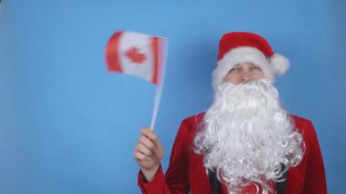 Mavi arka planda Kanada bayrağı sallayan sakallı Noel Baba kostümlü bir adam. Dünyada yeni yıl tatili kavramı