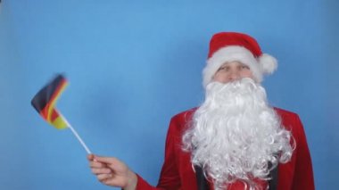 Mavi arka planda Almanya bayrağı sallayan, sakallı, Noel Baba kostümlü bir adam. Dünyada yeni yıl tatili kavramı