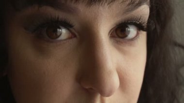 Uzun takma kirpikli, kahverengi gözlü ve siyah saçlı bir kadın kameraya bakıyor. Moda makyajlı güzel esmer kız modeli. Doğal ve temiz ten rengi.