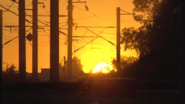 Demiryolu seviyesi Sunset 'ten siluetle geçiyor. Elektrikli demiryolu. Güneş ufukta görünüyor. Mesai bitiminde. Tren kazası ya da felaket için tehlikeli yol bölümü