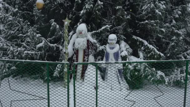 Zabawki Świętego Mikołaja lub Ded Moroz i Snegurochka są w śniegu w pobliżu choinki na głównym placu miasta w dzień po południu w śnieżycy. Sylwester w mieście w śnieżycy w spowolnieniu — Wideo stockowe