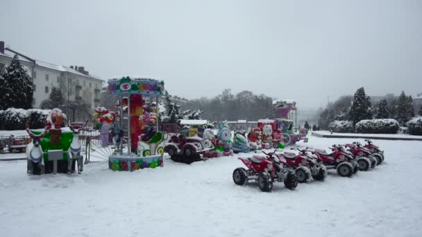 Attrazioni per bambini e gite sono in nevicata sulla piazza centrale della città nel pomeriggio. Capodanno in città con brutto tempo. Inizio vacanze e festeggiamenti in bufera in slow mo — Video Stock