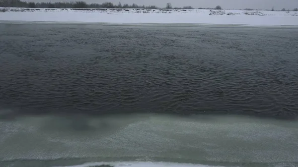 River flows in winter and snowing, ice along the edges of the bank in daytime. Nature background. Dangerous water for fishing — Stock Photo, Image