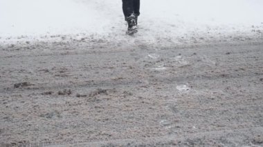 Yayaların bacakları kışın karlı bir yoldan gündüz vakti ağır çekimde geçer. Trafik ve kar fırtınası için kötü hava koşulları. Seyahatler için tehlike. Yerdeki camsı siyah buz