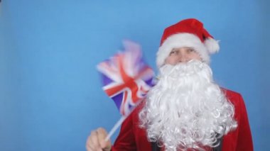 Mavi arka planda Britanya bayrağı sallayan sakallı Noel Baba kostümlü bir adam. Dünyada yeni yıl tatili kavramı