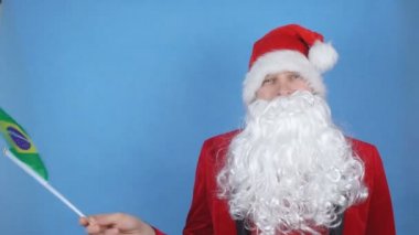 Mavi arka planda Brezilya bayrağı sallayan sakallı Noel Baba kostümlü bir adam. Dünyada yeni yıl tatili kavramı