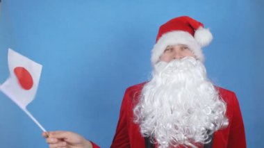Mavi arka planda Japon bayrağı sallayan, sakallı, Noel Baba kostümlü bir adam. Dünyada yeni yıl tatili kavramı