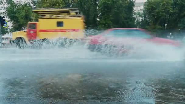 Auto 's rijden op een weg overspoeld met water, spray en fontein van onder de wielen bij regenachtig weer in de stad. Slechte en gevaarlijke omstandigheden voor het verkeer. Handheld schieten — Stockvideo