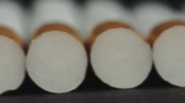 Sigara kuyruklarının arkasının makro görüntüsü. Arka filtreleri kapatın. Sigara içilmiyor. Birçok yeni sigara koyu siyah arka planda yatar. Kamera slaytları