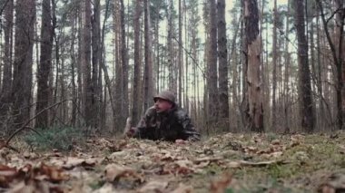 Kamuflaj kıyafeti giymiş yabancı bir avcı asker gibi yerde sürünüyor. Ordu parodisi. Orman bekçisi maskaralık yapıyor. Elinde tahta sopa olan adam. LSD narkotik etki, psikolojik bozukluk.