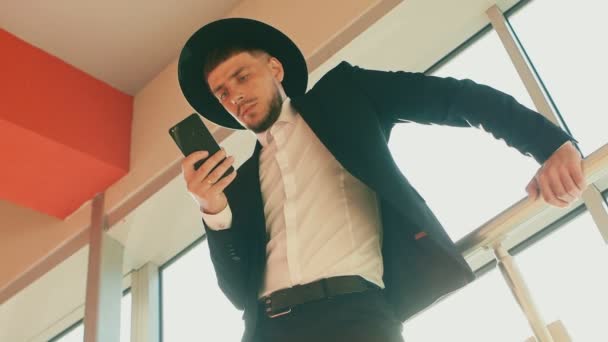 Hombre con camisa blanca, traje negro y sombrero. Persona decide sus propios asuntos en el teléfono inteligente. El hombre de negocios con barba y bigote parece judío o mafia italiana. Disparo de ángulo bajo, vista inferior . — Vídeos de Stock