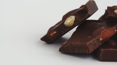 Makro shot, içinde badem fıstığı olan kırık çikolata parçaları paketsiz beyaz arka planda. İzole edilmiş. Kalori ve şeker. Tatlı ve lezzetli bir tatlı. Diyet ve sağlıksız yiyecekler
