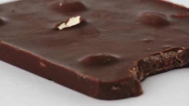 Macro shot, barra de chocolate con leche mordida con almendras enteras nueces está sobre fondo blanco sin embalaje. Concepto de dieta y alimentos poco saludables. Dulce cacao delicioso postre. Aislado. Calorías y azúcar dulce — Vídeo de stock