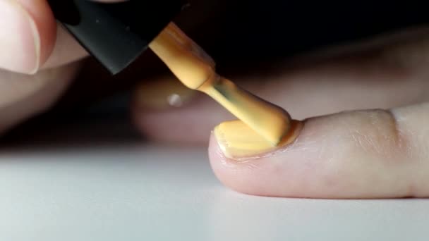 Девушка делает маникюр на ногтях, применяет оранжевый лак для ногтей, салон красоты, макро — стоковое видео