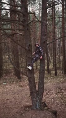Kamuflaj kıyafeti giymiş avcı orman bekçisi ağaçta oturuyor. Dikey çekim. Garip adamın kafası karışmış. LSD narkotik etkisi, psikolojik bozukluk konsepti. Psikedelik bir deli. Komik bir durum..