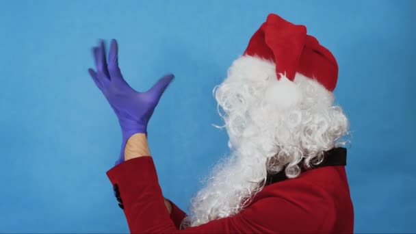 Christmas, New year and Coronavirus COVID концепція. Людина, як Санта Клаус в медичній захисній масці, одягає рукавички, повертає голову і дивиться в камеру. Пандемія — стокове відео