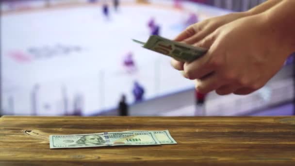 En man räknar pengar mot bakgrund av en hockeymatch som är på TV. Koncept för bookmakers och sportspel — Stockvideo
