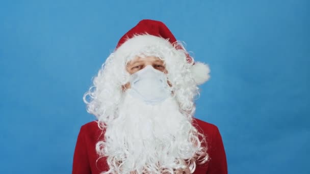 Natale, Capodanno e Coronavirus COVID concetto. Un uomo come Babbo Natale in maschera protettiva mostra segni di proibizione con l'indice. Ban gesto su sfondo blu — Video Stock