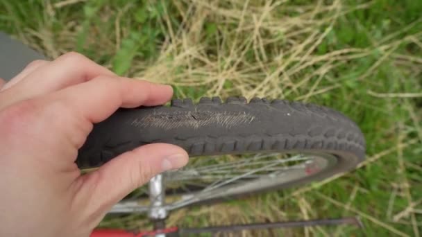 En cyklist inspekterar ett gammalt punkterat däck på ett cykelhjul, utomhus — Stockvideo