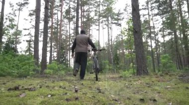 Kapüşonlu ve yelekli bir adam ormanda bisikleti yuvarlıyor. Bisiklet ve seyahat konsepti, yavaş çekim