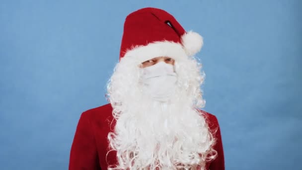 새해, 크리스마스, 코로나 바이러스 COVID 컨셉. 보호용 마스크를 쓰고 있는 산타 클로 오스 와 같은 사람이 장갑을 돌려 손으로 금하는 표시를 하고 있다. 항의의 표시. 세계적 유행병 — 비디오