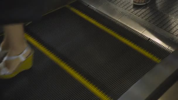 La gente se para en las escaleras mecánicas y baja. Los pies de las personas en los zapatos sobre la escalera mecánica, el primer plano, el fondo — Vídeo de stock