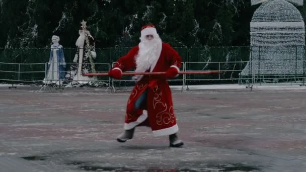 Russian Ded Moroz like a Santa Claus dances on city square near the Central Christmas tree. New year concept. Discounts and promotions, sales. Funny and comic situation — Stock Video