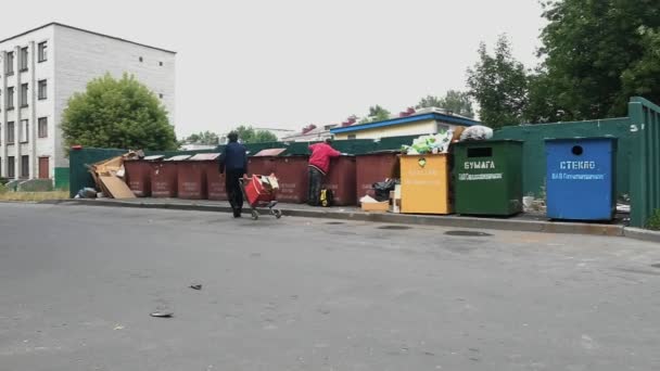 Нищие, бродяги и бедняки собирают и сортируют мусор в контейнерах с общественными отходами, мусорных баках летом. Бродяга. Бедность и выживание бездомных — стоковое видео