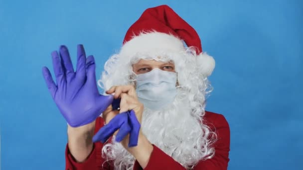 Muž jako Santa Claus v ochranné masce zvedne hlavu a nasadí si lékařské rukavice. Coronavirus COVID a Vánoce, novoroční koncept. Pandemie — Stock video