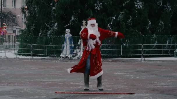 Русский Дед Мороз, как Санта Клаус танцует на городской площади возле центральной елки. Новогодняя концепция. Скидки и акции, продажи. Смешная и комическая ситуация — стоковое видео