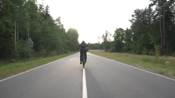 Mężczyzna z plecakiem na plecach jeździ rowerem po autostradzie na tle lasu, hobby — Wideo stockowe
