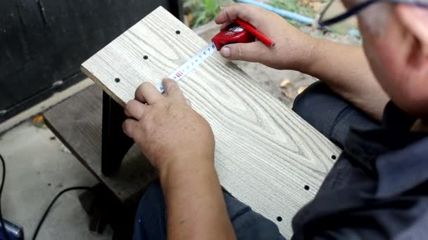Fabrication de meubles dans le pays, un homme âgé mesure avec un ruban à mesurer et fait des marques avec un crayon. Fait à la main — Video