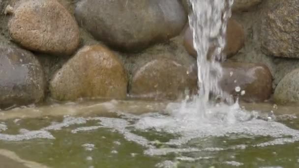 Het water stroomt van de stenen in de vijver. Kleine kunstmatige waterval, rust en meditatie, achtergrond voor tekst, slow motion — Stockvideo