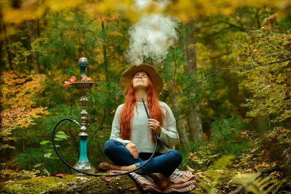 Unga rödhårig kvinna röka vattenpipa i skogen — Stockfoto