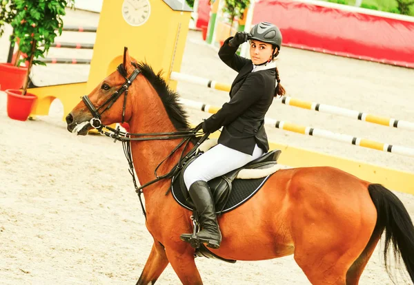 Beautiful girl on sorrel horse in jumping show, equestrian sports. Light-brown horse and young woman in uniform going to jump.