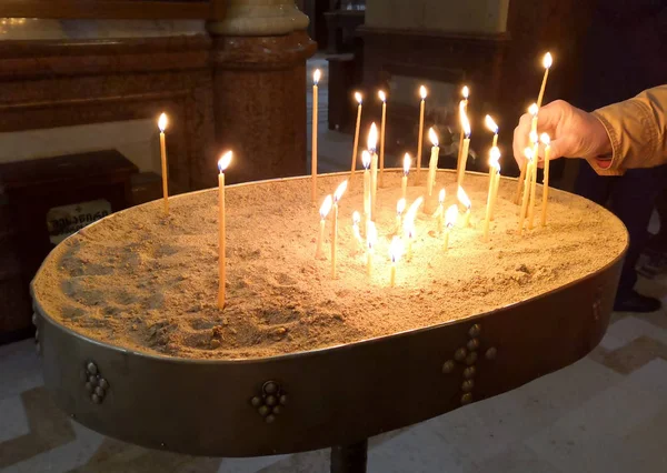 Candle Holder In The Church filled with sand. Hand with candle. The Holy Trinity Cathedral of Tbilisi commonly known as Sameba is the main cathedral of the Georgian Orthodox Church located in Tbilisi, the capital of Georgia. April, 20, 2019.