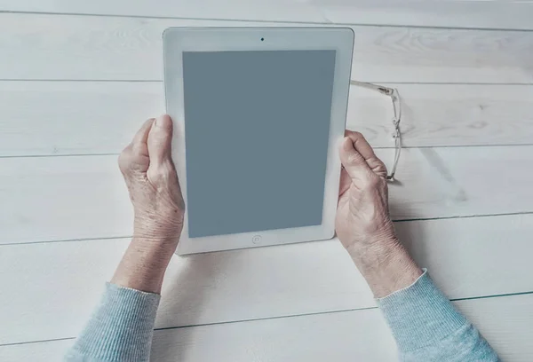 Old wrinkled hands holding tablet, empty screen. Elderly woman using digital tablet showing something on display, light background. Template, copy space mock-up. Technologies for seniors concept.