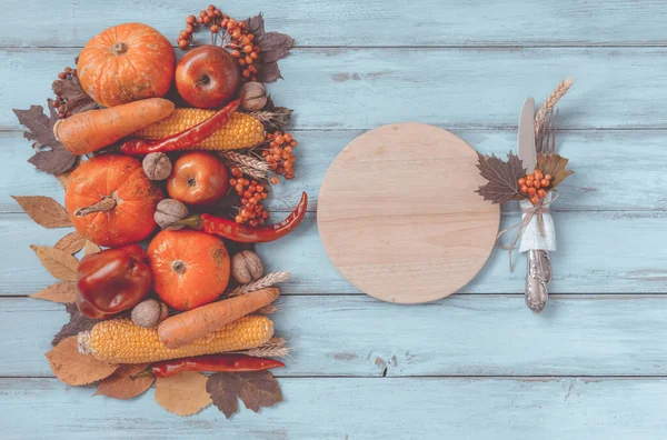Autumn background set, fallen leaves, fruits, vegetables, wooden table. Seasonal side composition, vintage round cutting board, copy space. Thanksgiving food, healthy and fresh, top view, flat lay.