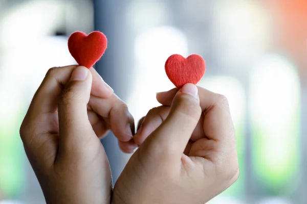 Tutan bir çift kırmızı kalp, seçici odak eller.