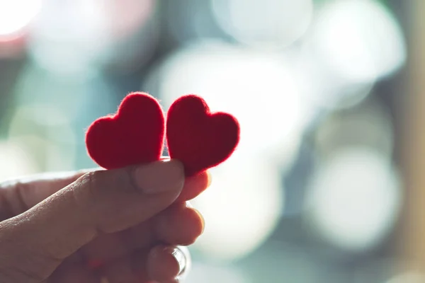 Tutan bir çift kırmızı kalp, seçici odak eller.