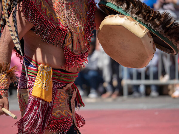 A man dressed in traditional Aztec garb beats on a drum during a march
