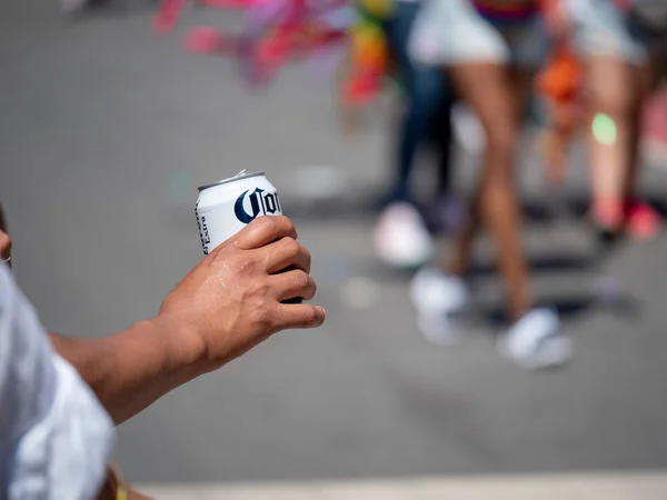La mano del hombre bebiendo lata de Corona enlatada en un entorno urbano festivo — Foto de Stock