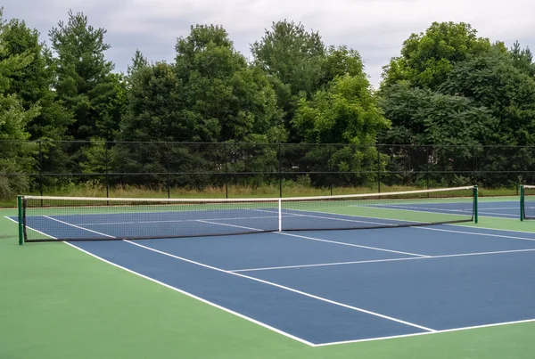 Pequeña cancha de tenis de asfalto azul rodeada de verde — Foto de Stock