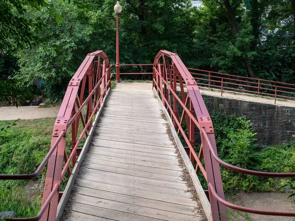 Estrecho puente de madera con protectores de acero rojo que conduce al sendero alrededor del área del canal — Foto de Stock