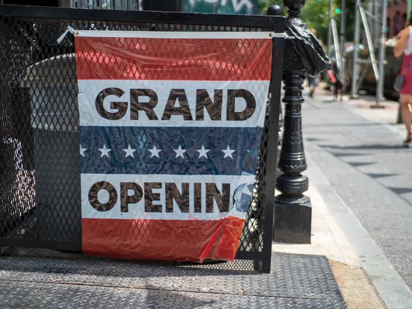 Makeshift grand opening sign hanging outside storefront on street