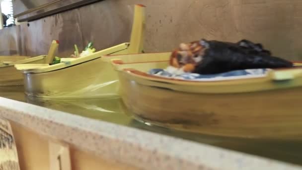 Verschiedene Sushi-Rollen kommen in Sushi-Booten in einer Sushi-Location am Band vorbei — Stockvideo