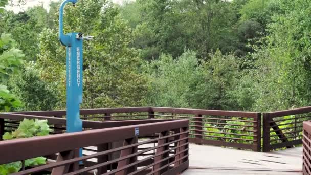 Noodgevallen blauwe telefoon paal langs een geïsoleerde houten wandelpad in rustige bos — Stockvideo