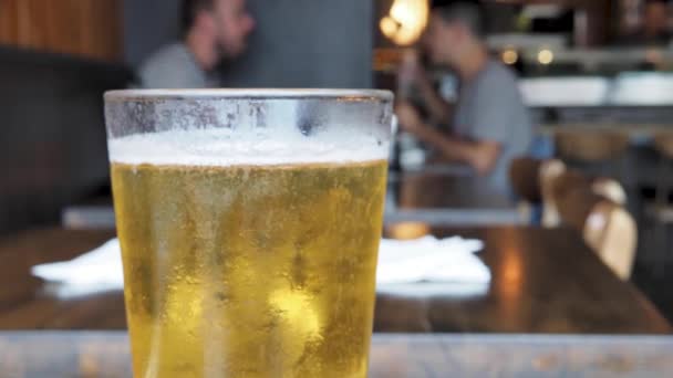 Frisch gegossenes Glas leichtes Lagerbier sprudelt oben auf dem Glas in einem Restaurant, in dem Menschen speisen — Stockvideo