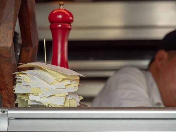 Stack of receipts on diner serving counter with cook working behind